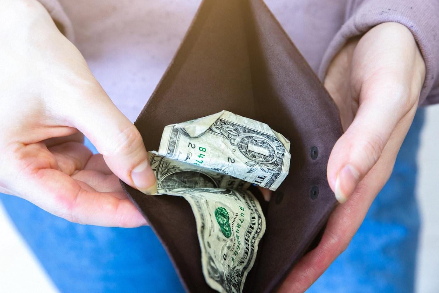 Empty wallet held open in both hands with a crumpled dollar bill inside, illustrating shrinking purchasing power